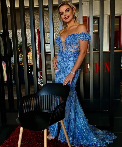 A woman wearing an off-the-shoulder blue lace evening gown.