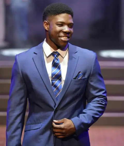 A man wearing a blue suit, white shirt and a blue and gold striped tie.