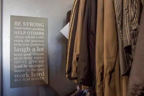 Garments hanging inside the shop beside a framed motivational sign.