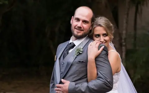 A couple together, wearing a grey formal suit and a white wedding dress.